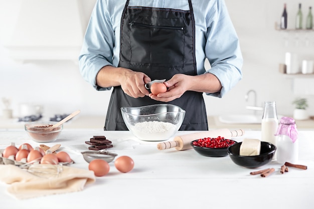 Um cozinheiro em uma cozinha rústica. As mãos masculinas com ingredientes para cozinhar produtos de farinha ou massa, pão, bolos, torta, bolo, pizza