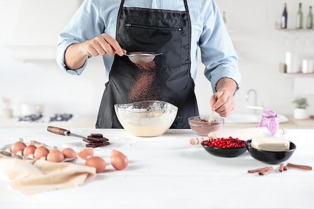 Um cozinheiro em uma cozinha rústica. As mãos masculinas com ingredientes para cozinhar produtos de farinha ou massa, pão, bolos, torta, bolo, pizza
