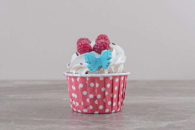 Um cupcake com cobertura de creme e frutas silvestres em mármore