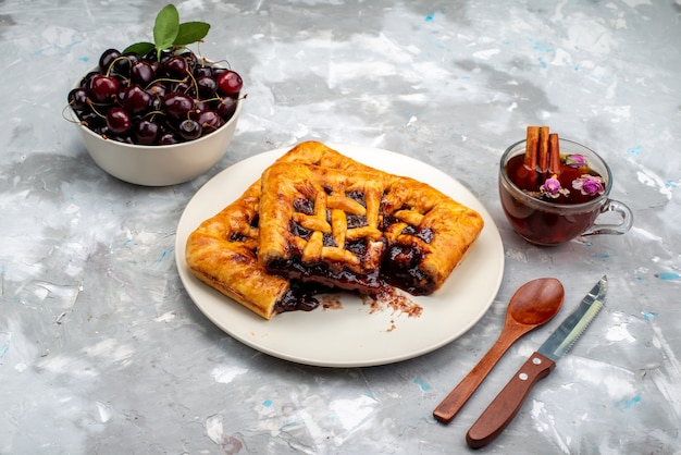 Foto grátis um delicioso bolo de cereja e frutado dentro de um prato branco com cerejas junto com chá na mesa escura de bolo de biscoito de frutas