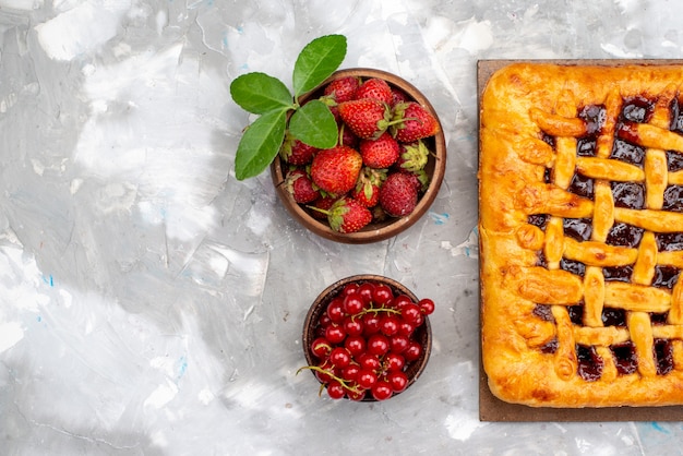 Um delicioso bolo de morango com geléia de morango dentro, junto com morangos frescos e cranberries na mesa de sobremesa cinza