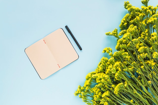 Um diário em branco aberto com caneta e flores amarelas em fundo azul