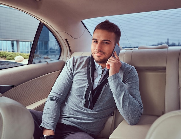 Um empresário bonito em roupas elegantes trabalhando, falando ao telefone enquanto está sentado no carro.