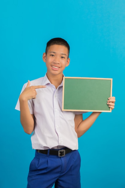 Um estudante do sexo masculino asiático masculino com um gesto das mãos levantadas e apontadas com uma placa verde segurando a outra mão no azul.