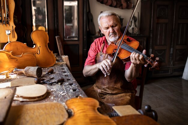 Um experiente marceneiro de cabelos grisalhos, usando avental de couro e sentado em sua oficina de marcenaria tocando violino