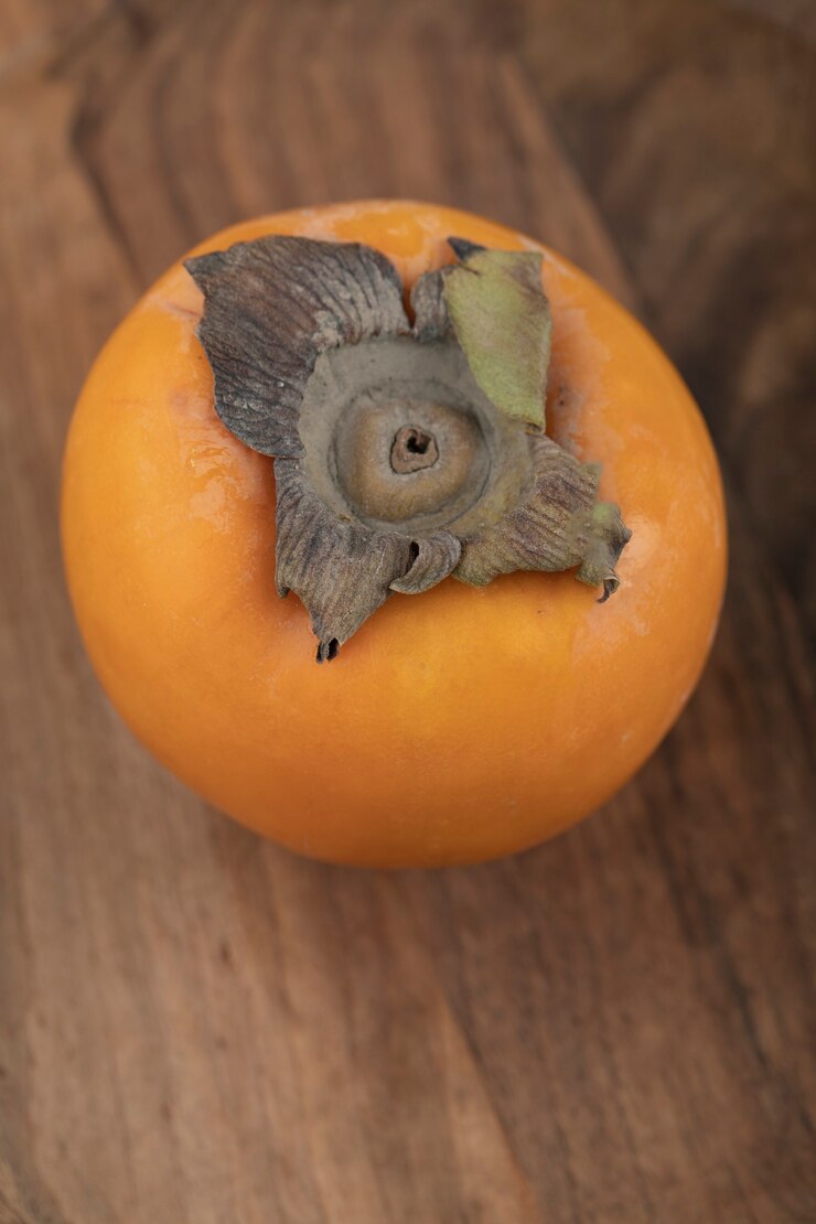 Foto grátis um fruto de caqui maduro colocado em uma superfície de madeira
