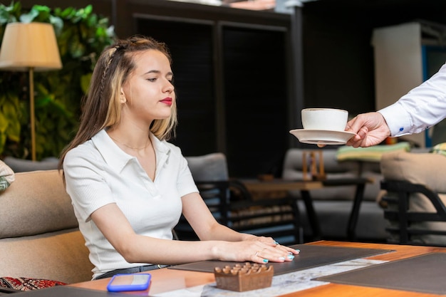 Um garçom dando uma xícara de café para a jovem no restaurante