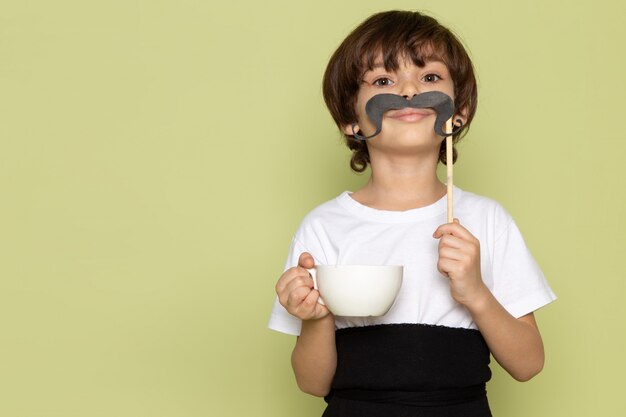 Um garoto de vista frontal com bigode e xícara de café em camiseta branca no chão de pedra colorida