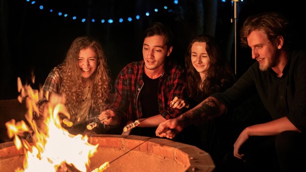 Um grupo de jovens amigos felizes perto de uma fogueira em uma noite glamping