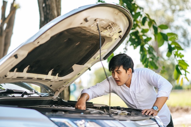 Um homem abre o capô de um carro para consertar o carro devido a uma avaria.