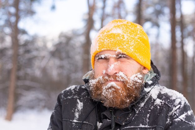 Um homem adulto com barba em uma floresta de inverno todo o rosto na neve, congelado, infeliz com o frio