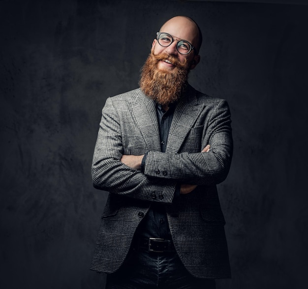 Um homem aristocrático barbudo ruiva elegante vestido com um terno e óculos sobre fundo cinza.