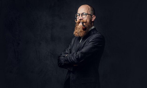 Um homem aristocrático barbudo ruiva elegante vestido com um terno e óculos sobre fundo cinza.