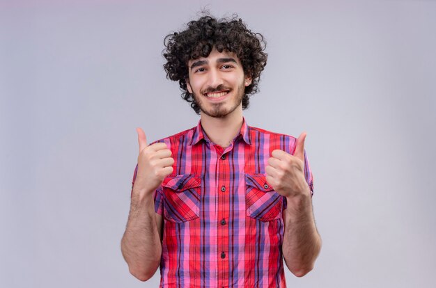 Um homem bonito e feliz com cabelo encaracolado e camisa xadrez mostrando os polegares para cima