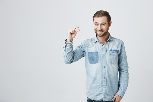 Um homem bonito sorri para a câmera mostra algo pequeno.