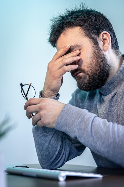 Um homem cansado esfrega os olhos na frente de uma tela de computador