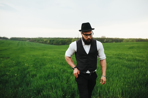 Um homem com barba e óculos escuros caminhando no campo