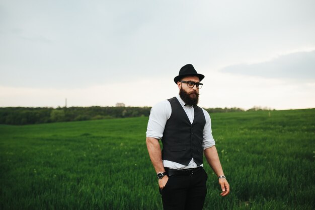 Um homem com barba e óculos escuros caminhando no campo