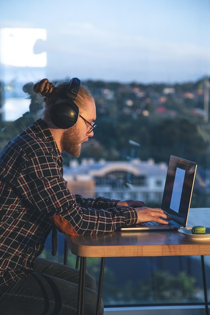 Foto grátis um homem com barba trabalha em um computador sentado no escritório perto da janela