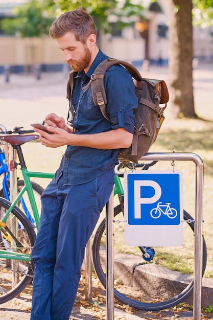 Um homem com smartphone perto da área de estacionamento de bicicletas.