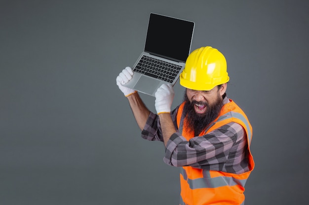 Um homem de engenharia usando um capacete amarelo segurando um caderno em um cinza.