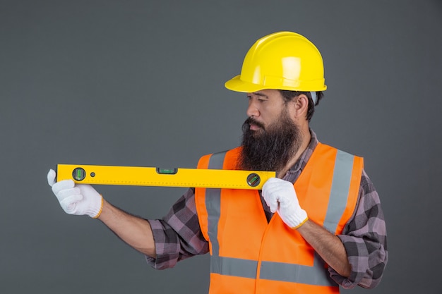 Um homem de engenharia usando um capacete amarelo segurando um medidor de nível de água em um cinza.