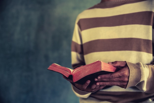 um homem de pé durante a leitura da Bíblia ou livro sobre a parede de concreto com luz de janela