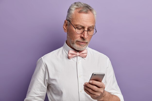 Um homem elegante sênior trabalhando em seu telefone, concentrado na tela, tenta entender como usar as tecnologias modernas