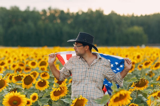 Um homem está entrando no campo de girassóis com a bandeira dos estados unidos. conceito do dia da independência de 4 de julho.