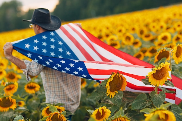 Um homem está entrando no campo de girassol com a bandeira americana. conceito do dia da independência de 4 de julho.