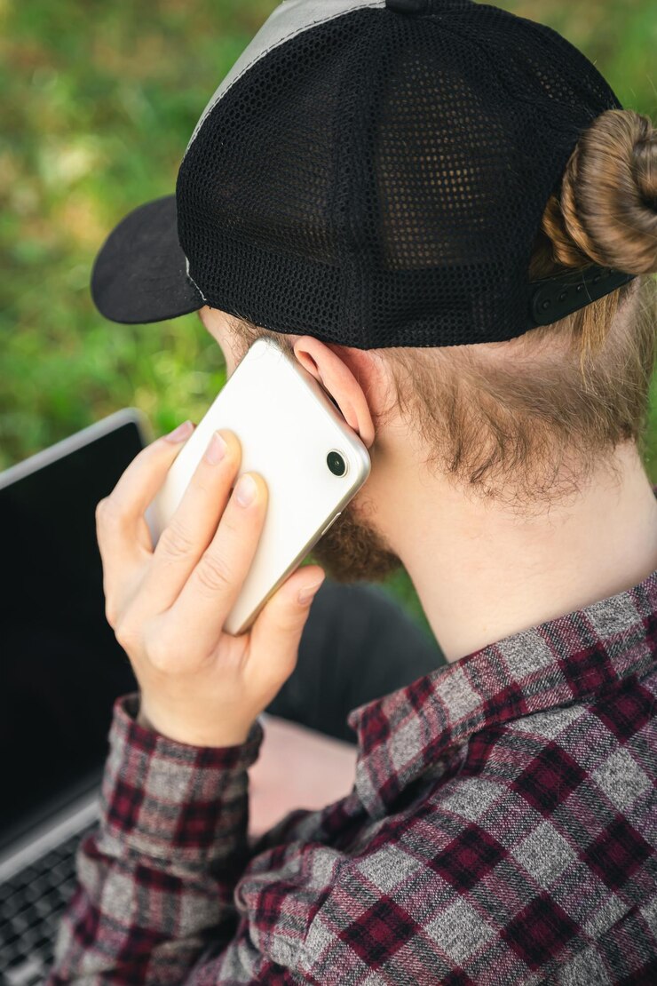 Foto grátis um homem está falando em um smartphone enquanto está sentado na grama com um laptop