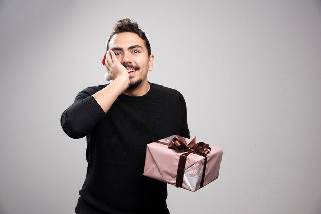 Um homem feliz com um chapéu de papai noel segurando um presente de ano novo.