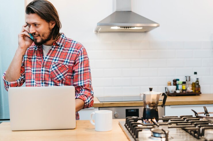 Foto grátis um, homem jovem, falando telefone móvel, com, laptop, e, xícara café, ligado, contador cozinha