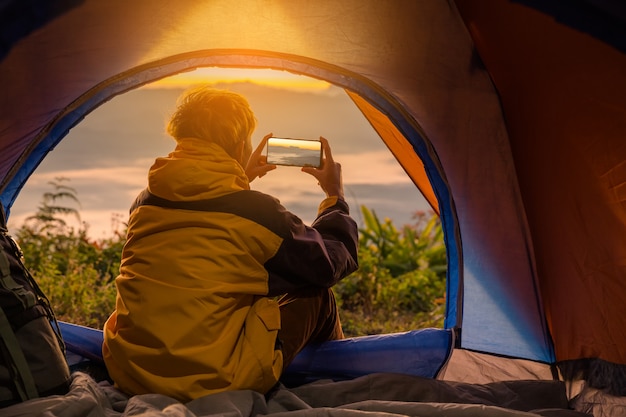 Um, homem jovem, sentando, em, a, barraca, com, levando, foto, com, um, telefone móvel