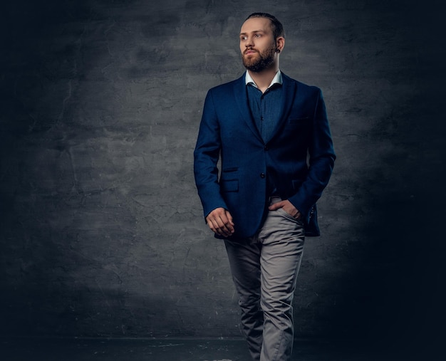 Um homem moderno barbudo elegante vestido de terno e óculos escuros sobre fundo cinza escuro.