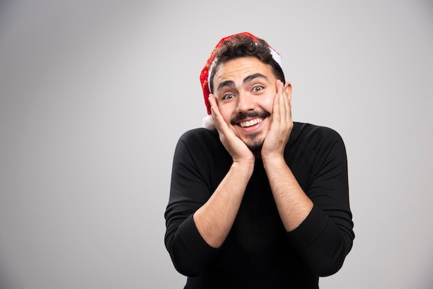 Um homem moreno sorridente com chapéu de papai noel em pé e posando