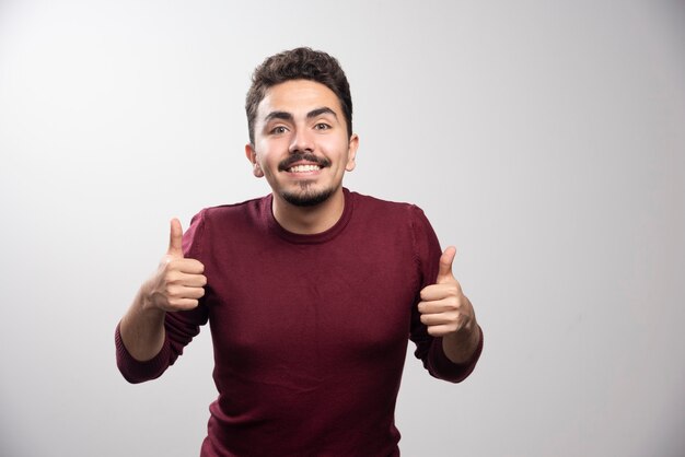 Um homem moreno sorridente mostrando os polegares para cima e de pé