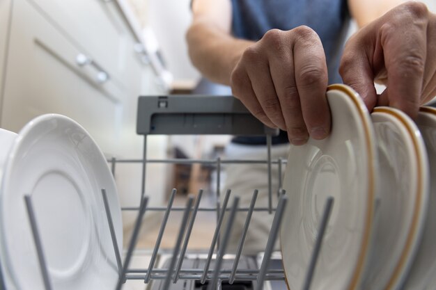 Um homem na frente de uma máquina de lavar louça tira pratos limpos após a lavagem.