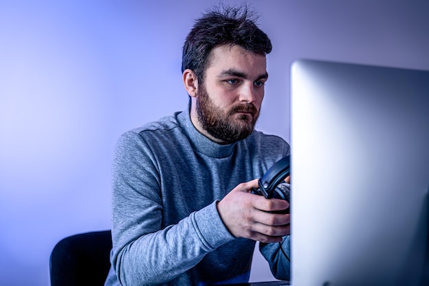 Um homem se senta na frente de um computador com fones de ouvido nas mãos