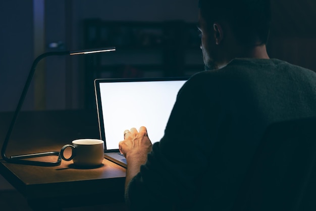 Foto grátis um homem senta-se em uma sala escura na frente de uma tela de laptop em branco