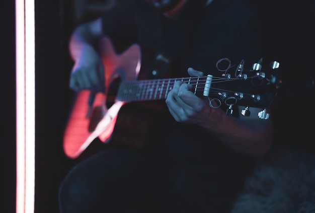 Um homem toca violão em um quarto escuro. Performance ao vivo, concerto acústico.
