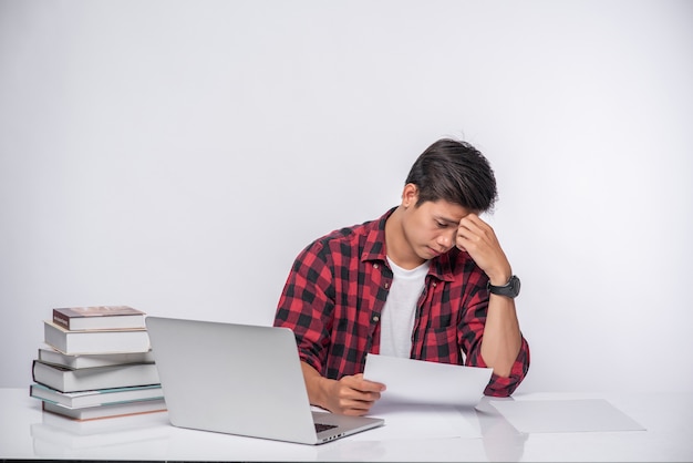 Um homem usando um laptop no escritório e fazendo uma análise de documentos.