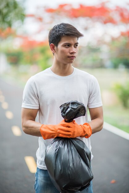 Um homem vestindo luvas laranja coletando lixo em um saco preto.