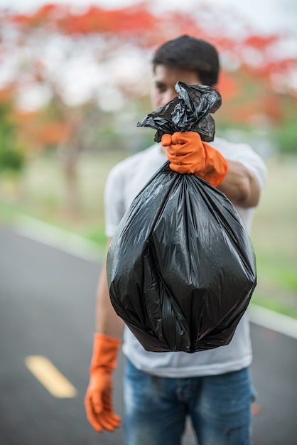 Um homem vestindo luvas laranja coletando lixo em um saco preto.