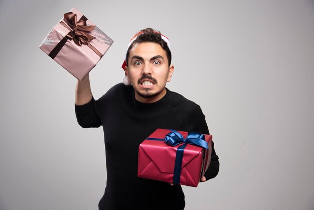 Um homem zangado com um chapéu de papai noel segurando um presente de ano novo.