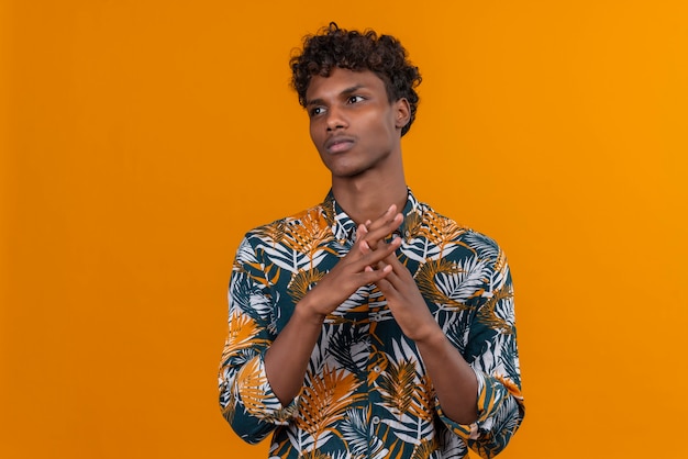 Foto grátis um jovem bonito de pele escura com cabelo encaracolado em uma camisa estampada de folhas olhando para o lado