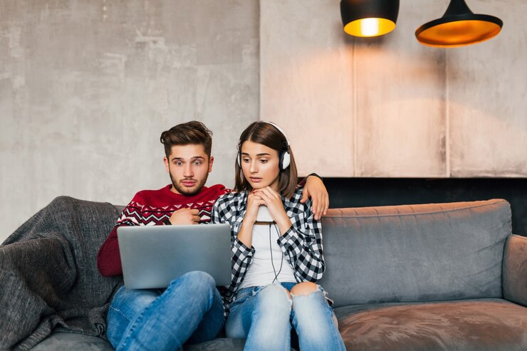 Foto grátis um jovem bonito e uma mulher sentada em casa no inverno olhando no laptop com uma expressão de rosto triste e chocado, com medo, assistindo a um filme de terror em um encontro, usando a internet, casal em momentos de lazer juntos, namorando