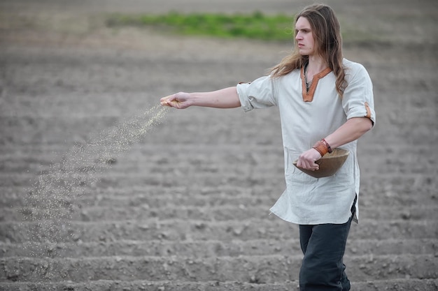 Um jovem camponês de aparência escandinava semeia o campo com grãos