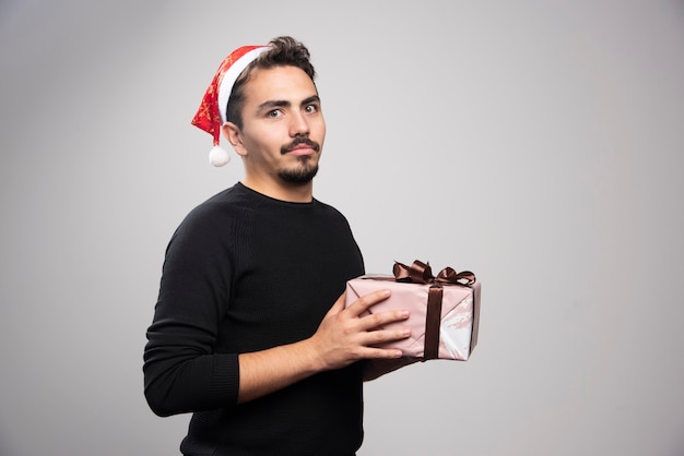 Um jovem com um chapéu de papai noel segurando um presente de ano novo.