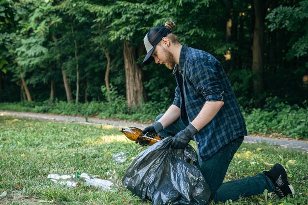 Um jovem com um saco de lixo na floresta limpa garrafas plásticas